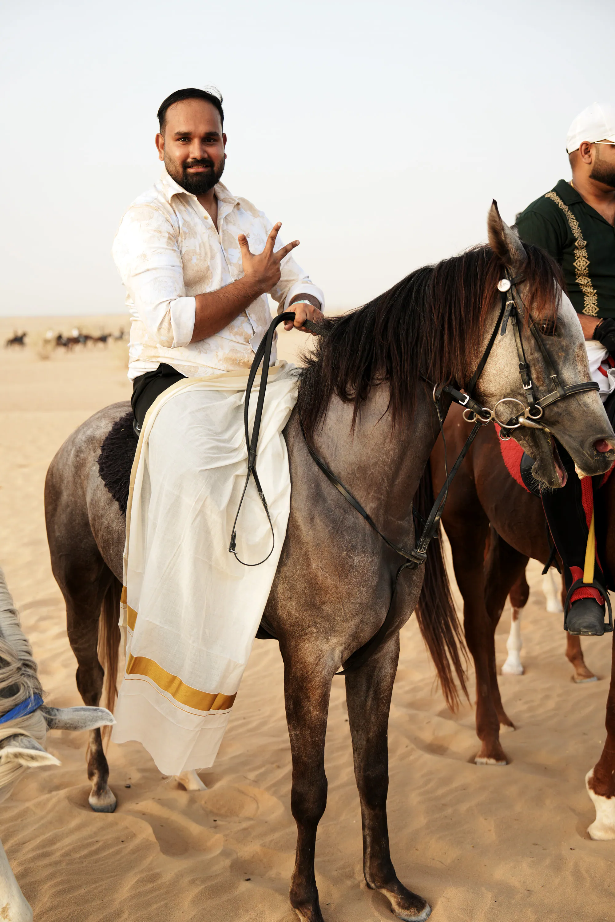 A rider in a white and gold Kerala mundu on a grey horse in the desert