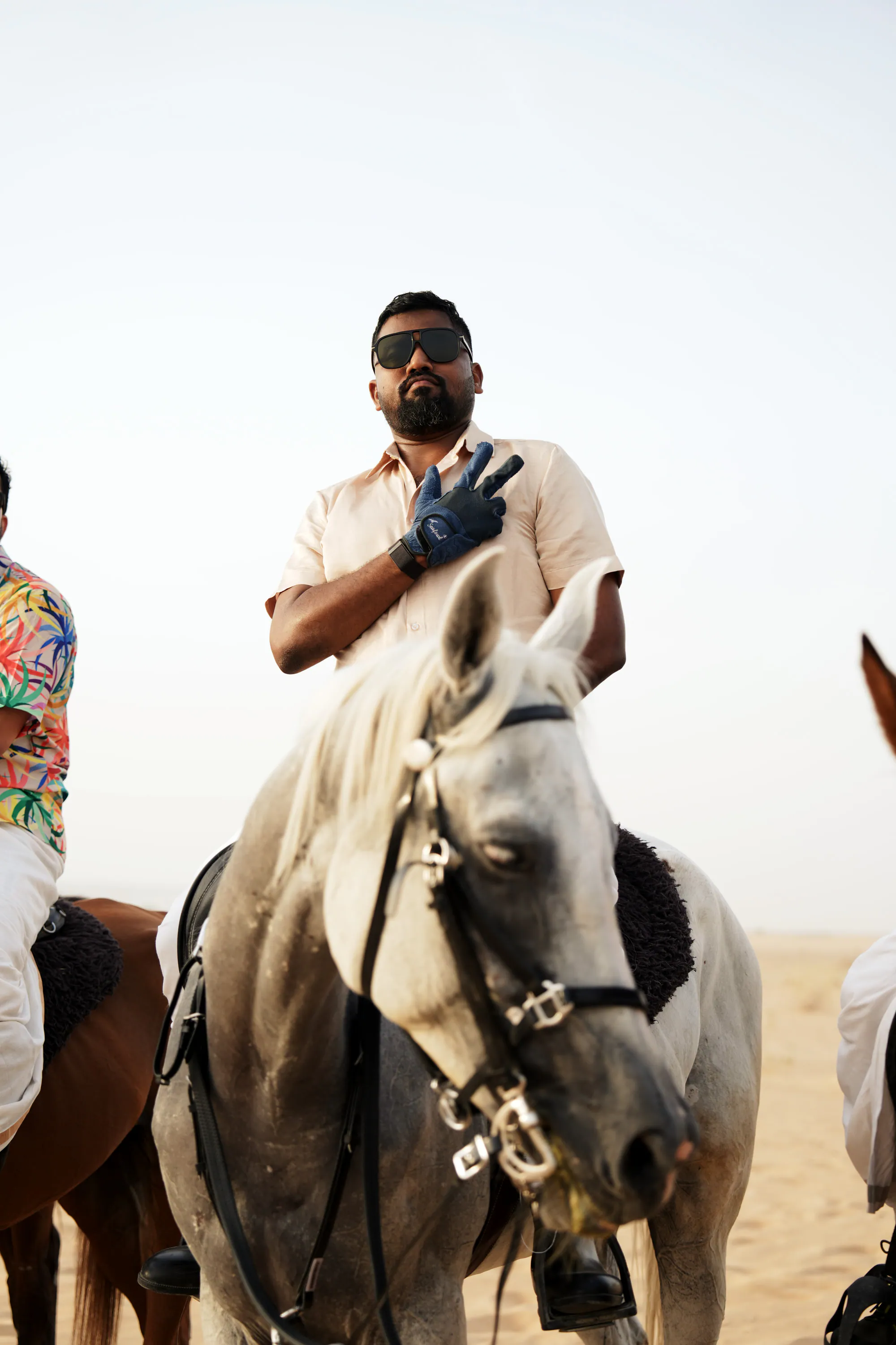A rider in sunglasses on a grey horse with his hand on his heart