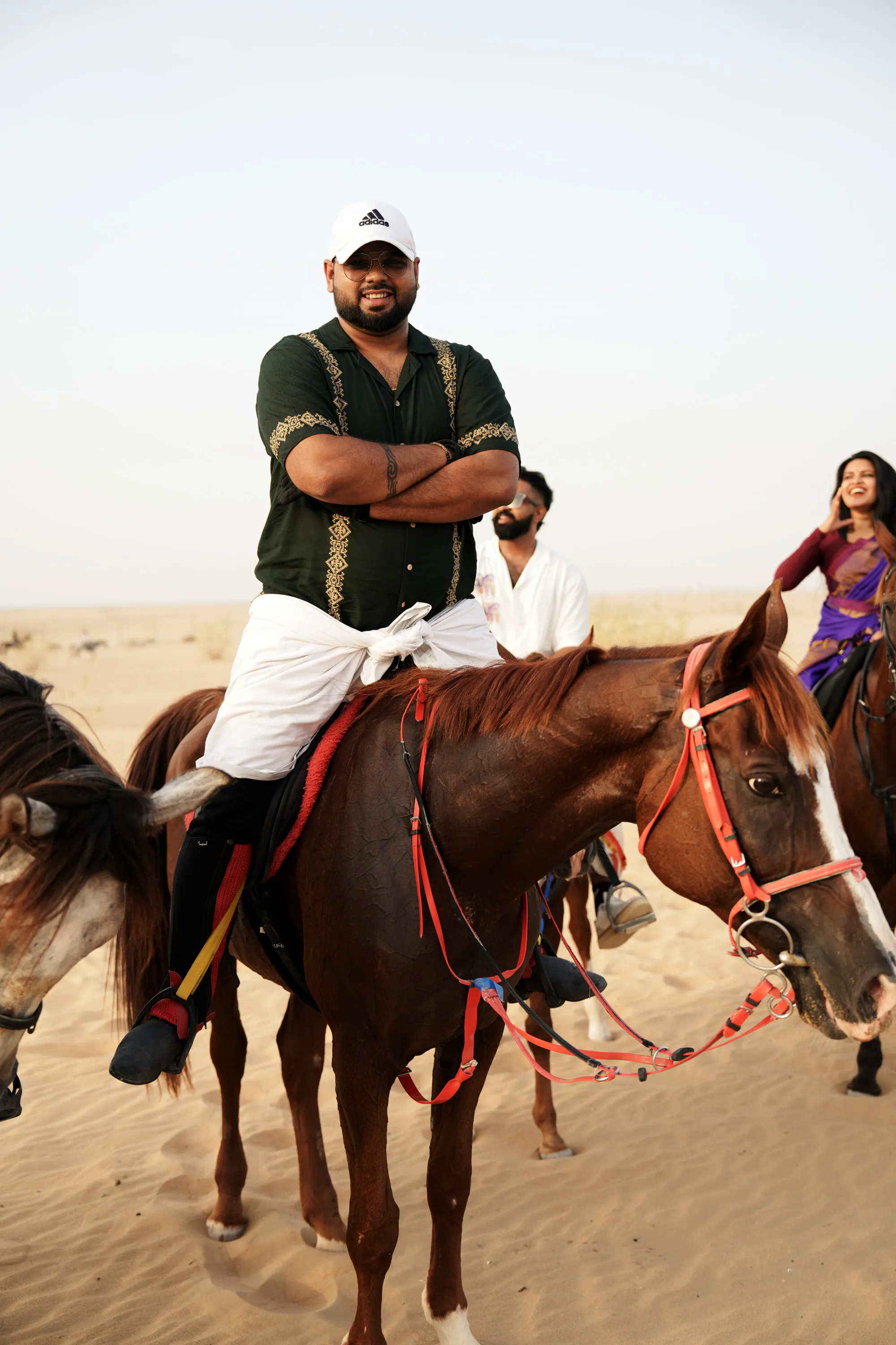 A rider with arms crossed on a chestnut horse in the desert