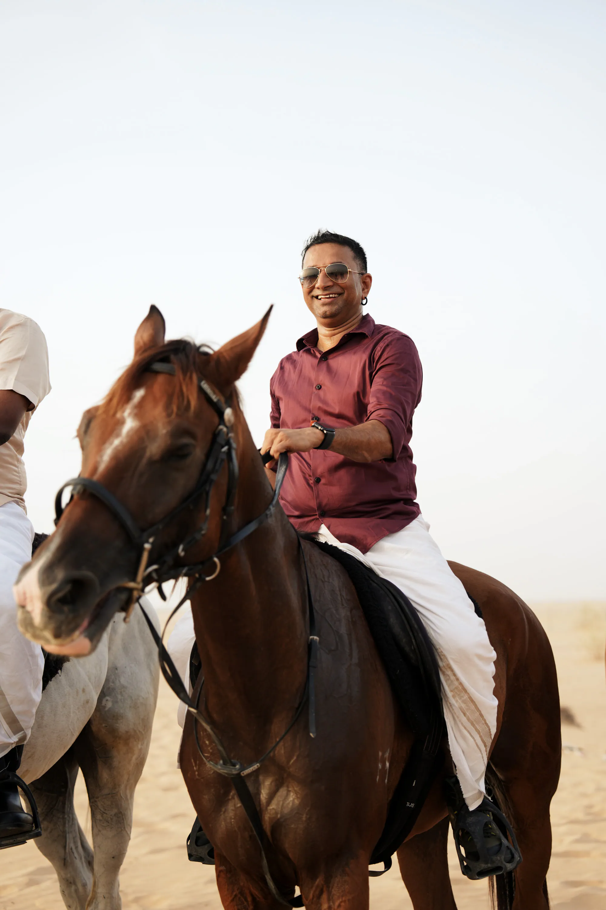 A smiling rider in a maroon shirt on a chestnut horse
