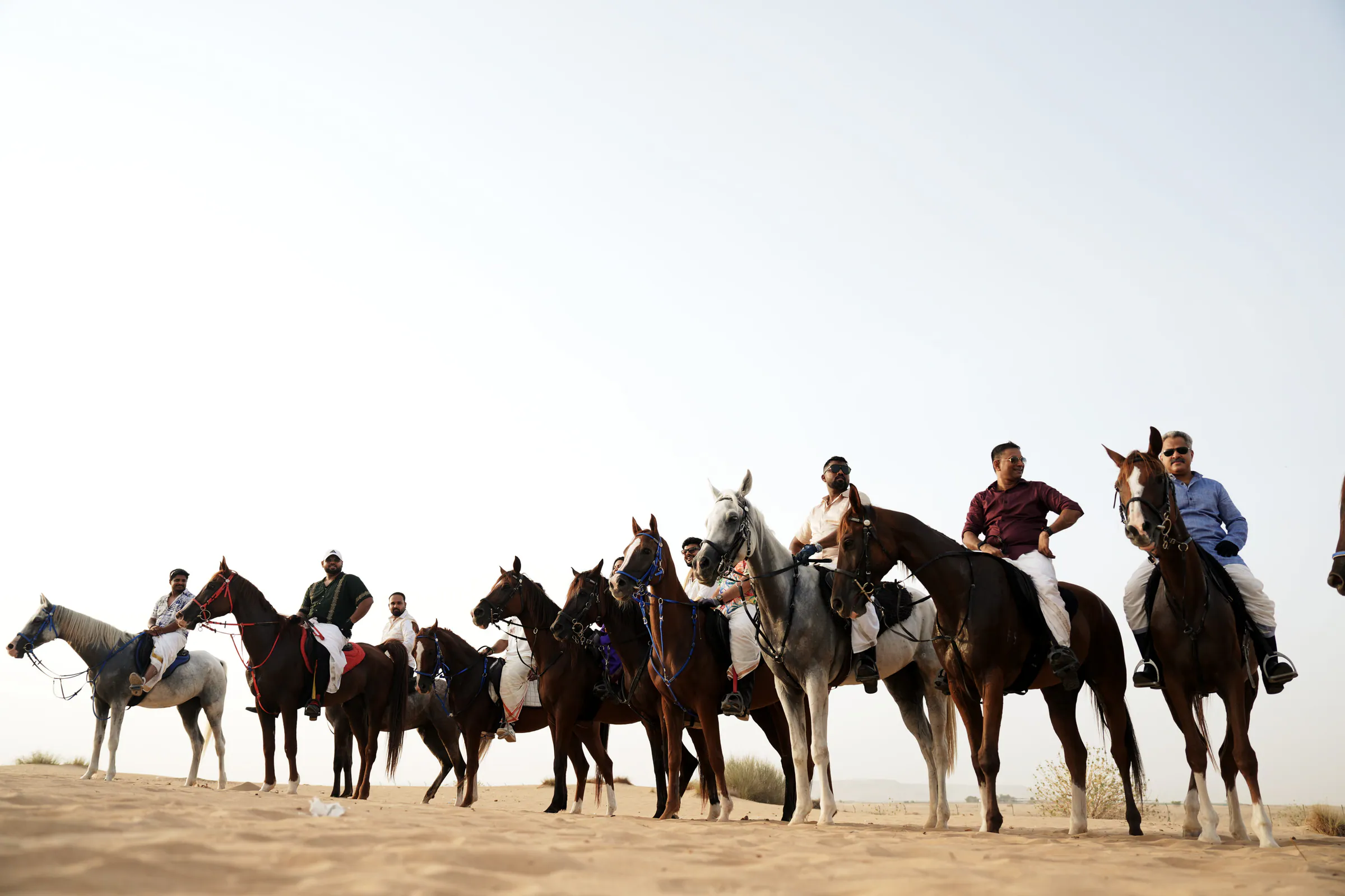 Riders lined up on horseback on a sandy ridge under a pale sky